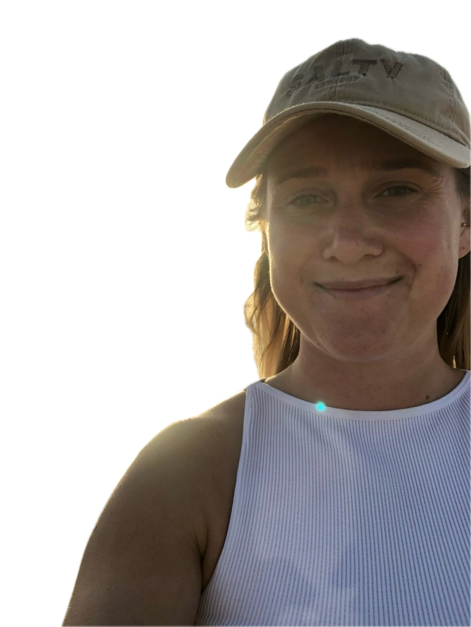 Nicole, a woman in a baseball cap and white tank top, smiling in warm sunset light