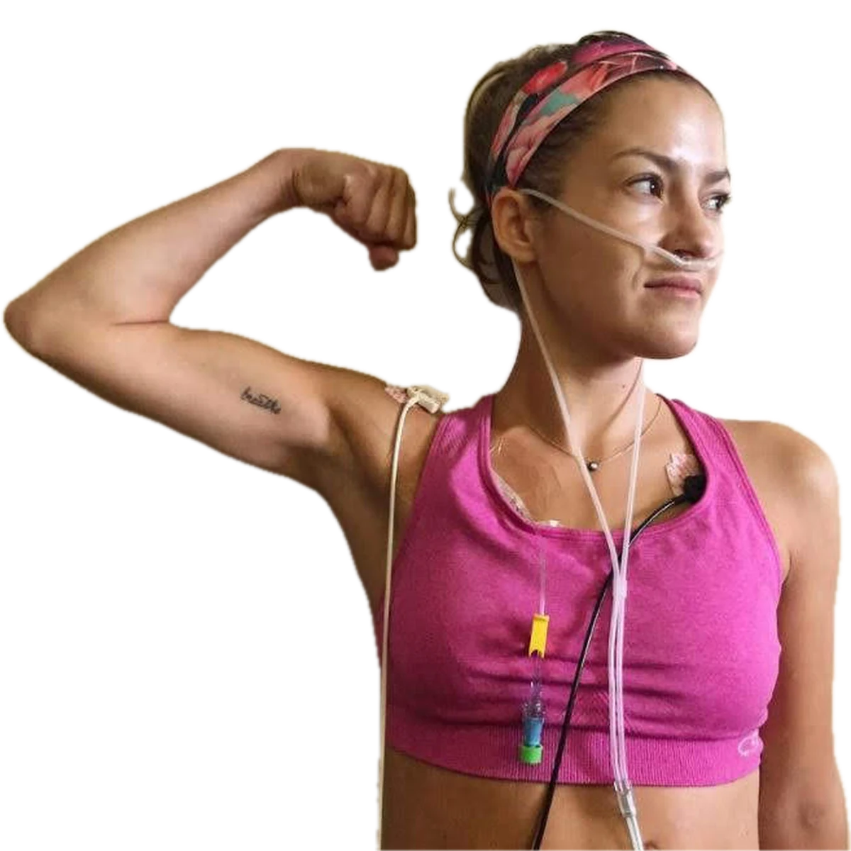 Caleigh flexing her bicep, wearing a pink sports bra and a floral headband, with an oxygen cannula and treatment lines