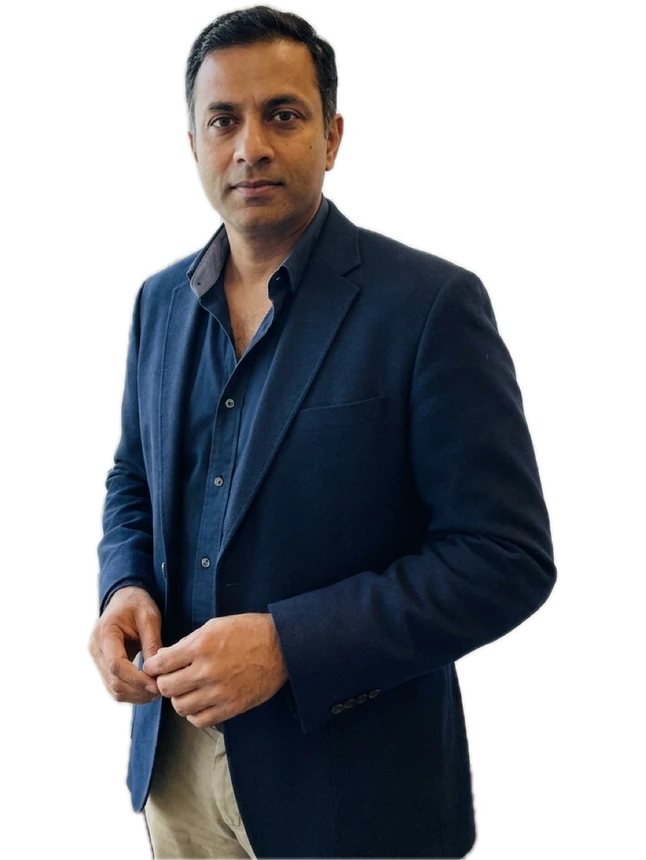 A man in a navy blazer standing with his hands clasped.